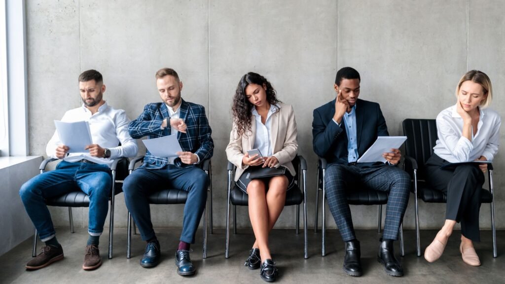 Cinque candidati seduti in fila in attesa del proprio turno prima di un assessment day per assistente di volo